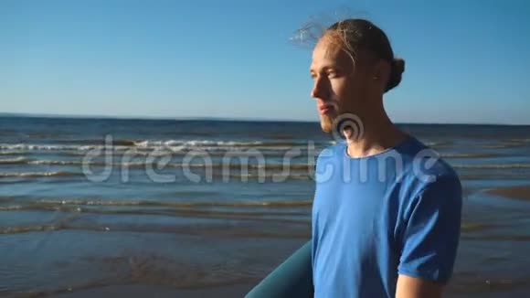 一个拿着瑜伽卷在沙滩上散步的男人视频的预览图