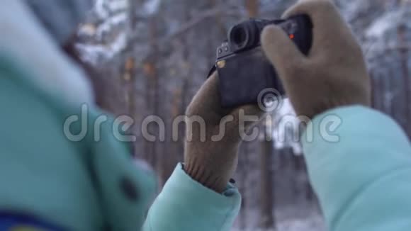 美丽的年轻女子穿着冬天的衣服手套和羊毛帽用针织相机拍摄雪林视频的预览图