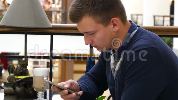 年轻的帅哥在购物中心的咖啡馆里使用智能手机特写人浏览信息和滚动视频的预览图