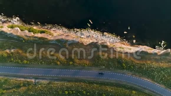 从上面的空中射击驾驶着黑色的汽车在海边的悬崖附近的农村公路旁的田野里视频的预览图