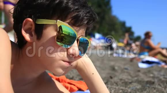 男孩是一个十几岁的孩子在海滩上戴着太阳镜海滩上有度假者戴着眼镜视频的预览图