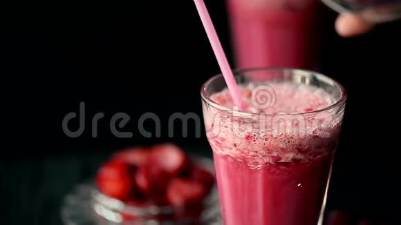 有一杯红冰沙里面有牛奶樱桃和草莓在黑暗中一块冰沙被倒入玻璃杯中视频的预览图