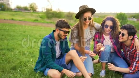 四个年轻的嬉皮士在田野里在夕阳下坐在绿草上闪闪发光视频的预览图