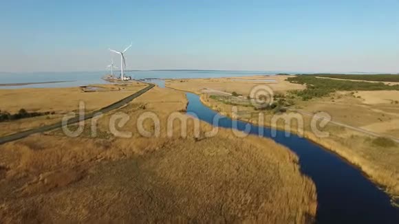 4K飞越蓝色河流和田野飞向靠近大海的风力涡轮机日落时的鸟瞰图视频的预览图