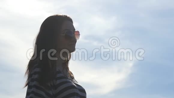 年轻的女人戴着太阳镜看着相机微笑着蓝天背景是云相当漂亮的形象视频的预览图