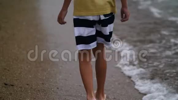 傍晚男孩正沿着沙滩上的金沙散步双脚特写视频的预览图