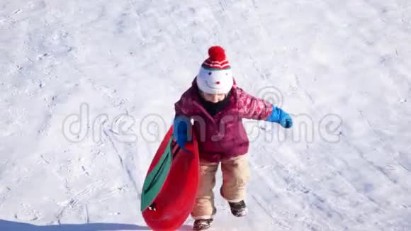 冬天散步的孩子一个女孩骑在塑料板上的雪滑板上视频的预览图