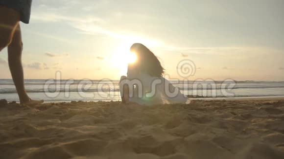 一个女人坐在海边的沙滩上享受美丽的日落和海洋年轻人上来坐下视频的预览图