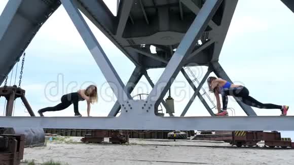 两个年轻的运动女性进行力量练习他们站在货运起重机的金属横梁上黎明时健身视频的预览图