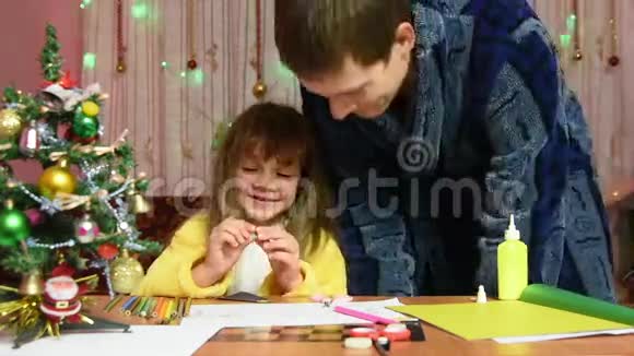 爸爸坐下来找她的女儿滑稽地扔下一瓶胶水帮她做圣诞工艺品视频的预览图
