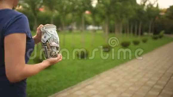 女人拿着一个玻璃罐子钱沿着一条城市街道跑概念金融折扣销售视频的预览图