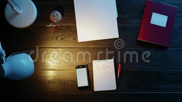 桌子旁的人用电话在笔记本上写东西旁边是文件夹灯球办公室和按钮视频的预览图