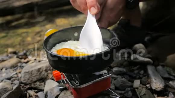 男人的手在野营炉子上用煎锅炒鸡蛋视频的预览图