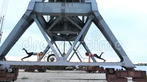 两个年轻的运动女性进行力量练习他们站在货运起重机的金属横梁上黎明时健身视频的预览图