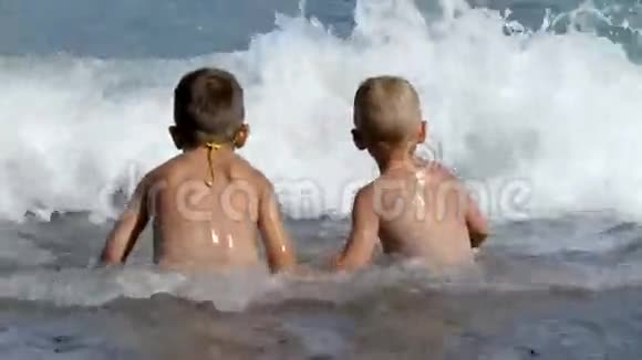 两个小男孩坐在沙滩上沐浴在海浪中视频的预览图