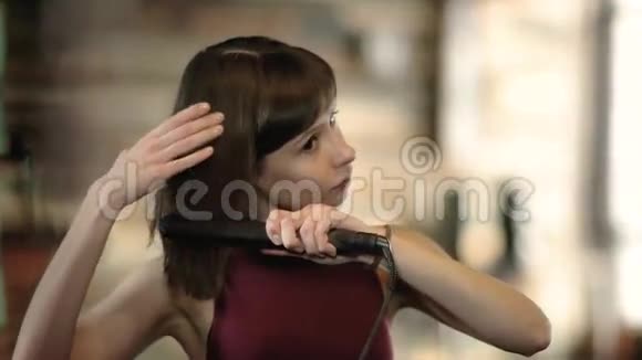 漂亮的年轻女子用铁把头发弄直视频的预览图