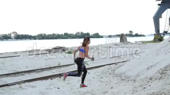 年轻女子运动员爬上一座沙山背景上可以看到河货鹤货港黎明视频的预览图