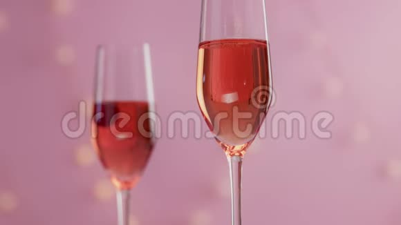 粉红色的起泡葡萄酒带有女士的手和带有圣诞灯的粉红色背景的眼镜视频的预览图