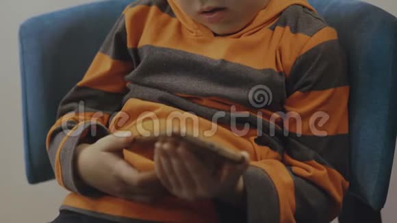 可爱的蹒跚学步的男孩坐在椅子上使用智能手机4K视频的预览图