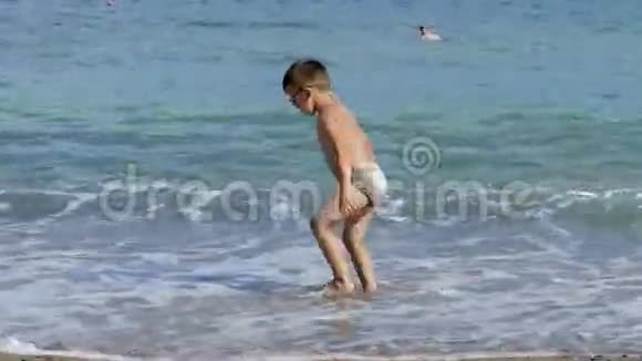 两个小男孩坐在沙滩上沐浴在海浪中视频的预览图