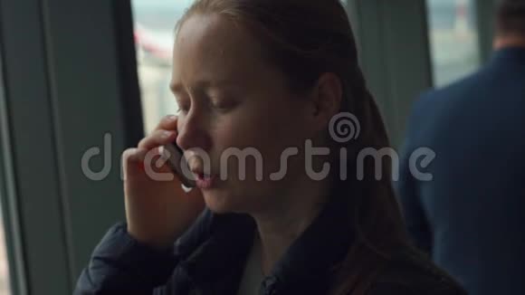 女青年在机场的一个大窗户前用手机说话视频的预览图