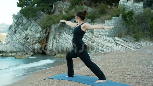 女人在海石背景下在瑜伽中表演战士的姿势视频的预览图