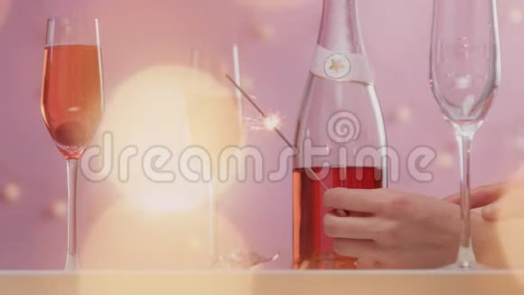 粉红色的起泡葡萄酒带有女士的手和带有圣诞灯的粉红色背景的眼镜视频的预览图