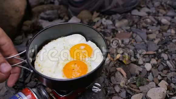 在河边的露营炉上人们用手在煎锅里炒鸡蛋视频的预览图