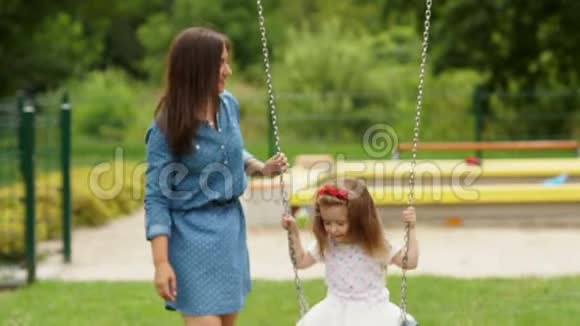 穿着蓝色短裙的神奇妈妈花时间和她的小女儿外出可爱的女孩骑着秋千视频的预览图