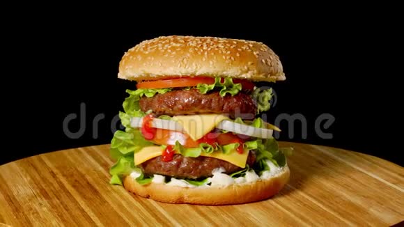 大汉堡配牛肉西红柿蘑菇和黄瓜配上融化的奶酪在黑色的木板上旋转视频的预览图
