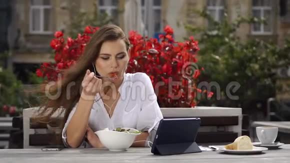 布鲁内特女士吃沙拉看着她的平板电脑上的东西而她坐在餐厅前红花视频的预览图