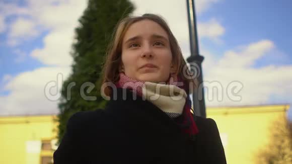 年轻快乐的时髦女孩在针叶树黄色建筑和蓝天的背景下与镜头交谈视频的预览图
