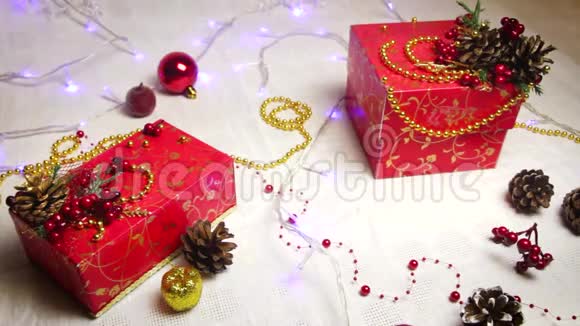 红色手工制作的礼品盒和圣诞装饰品金色的苹果和带有闪闪发光灯笼的凸起物俯视视频的预览图