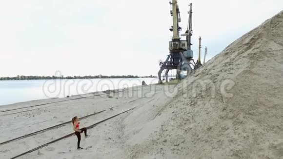 年轻女子运动员爬上一座沙山背景上可以看到河货鹤货港黎明视频的预览图