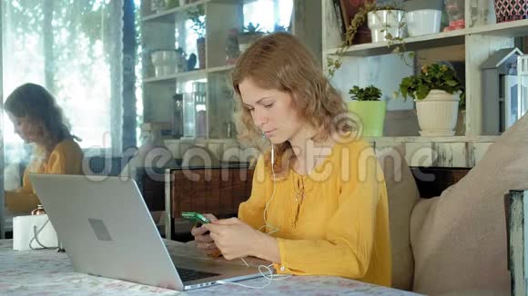 戴着现代笔记本电脑耳机的年轻女性坐在咖啡馆里视频的预览图