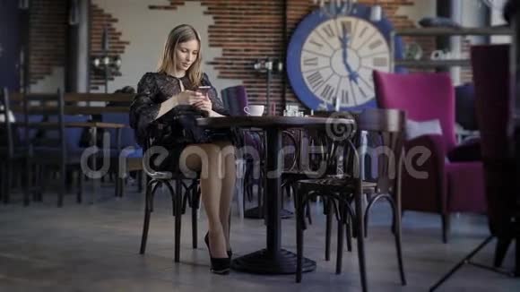 年轻可爱的女人用电话坐在咖啡馆里拿着智能手机接短信一位漂亮的商界女性视频的预览图