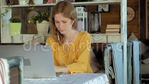 戴着现代笔记本电脑耳机的年轻女性坐在咖啡馆里视频的预览图