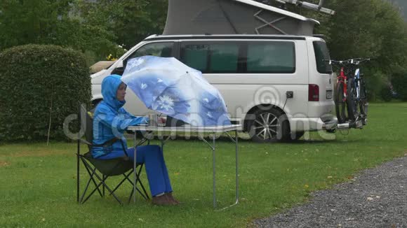 一个年轻的女人在雨下的伞下的野餐桌上工作视频的预览图