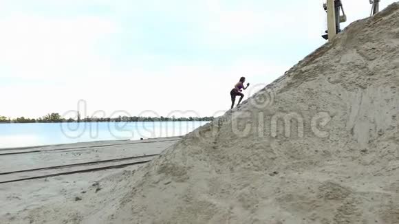 年轻女子运动员爬上一座沙山在背景上可以看到河货鹤货港黎明视频的预览图