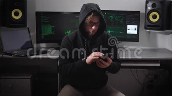 一个穿着夹克衫戴着引擎盖的人在电脑室戴着墨镜手上拿着智能手机的黑客视频的预览图