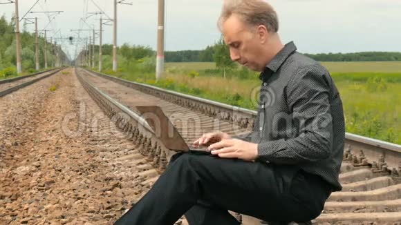 一个男人坐在铁轨上用笔记本电脑工作视频的预览图