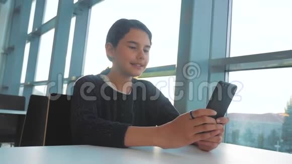 十几岁的女孩正在聊天在一张桌子阳光下在一个咖啡馆的生活方式中在一部智能手机中交流视频的预览图