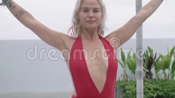 迷人的金发女人穿着红色泳衣在酒店的露天阳台上练习瑜伽视频的预览图