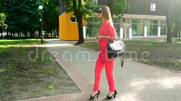 穿着红西装戴太阳镜的漂亮年轻商务女孩穿着高跟鞋走在街上视频的预览图