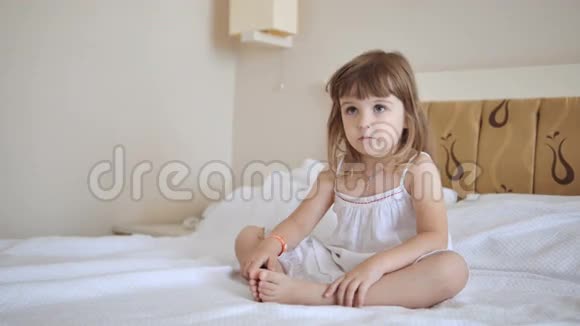 可爱的孩子穿着白色连衣裙在床上看电视视频的预览图