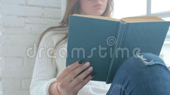 一个戴眼镜的年轻女孩正坐在窗台上看书视频的预览图