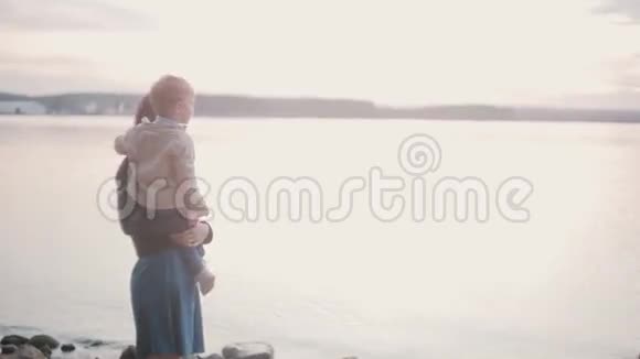 母亲牵着儿子的手在海滩的岸边女人和小男孩说话指着地平线视频的预览图