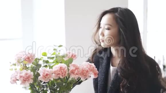 一个年轻的亚洲女人在家里的花瓶里闻到一朵粉红色的花视频的预览图