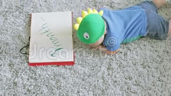 三个月的婴儿戴着一顶绿色的龙形帽子看着一本笔记本趴在地板上视频的预览图