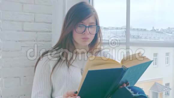 一个戴眼镜的年轻女孩正坐在窗台上看书视频的预览图